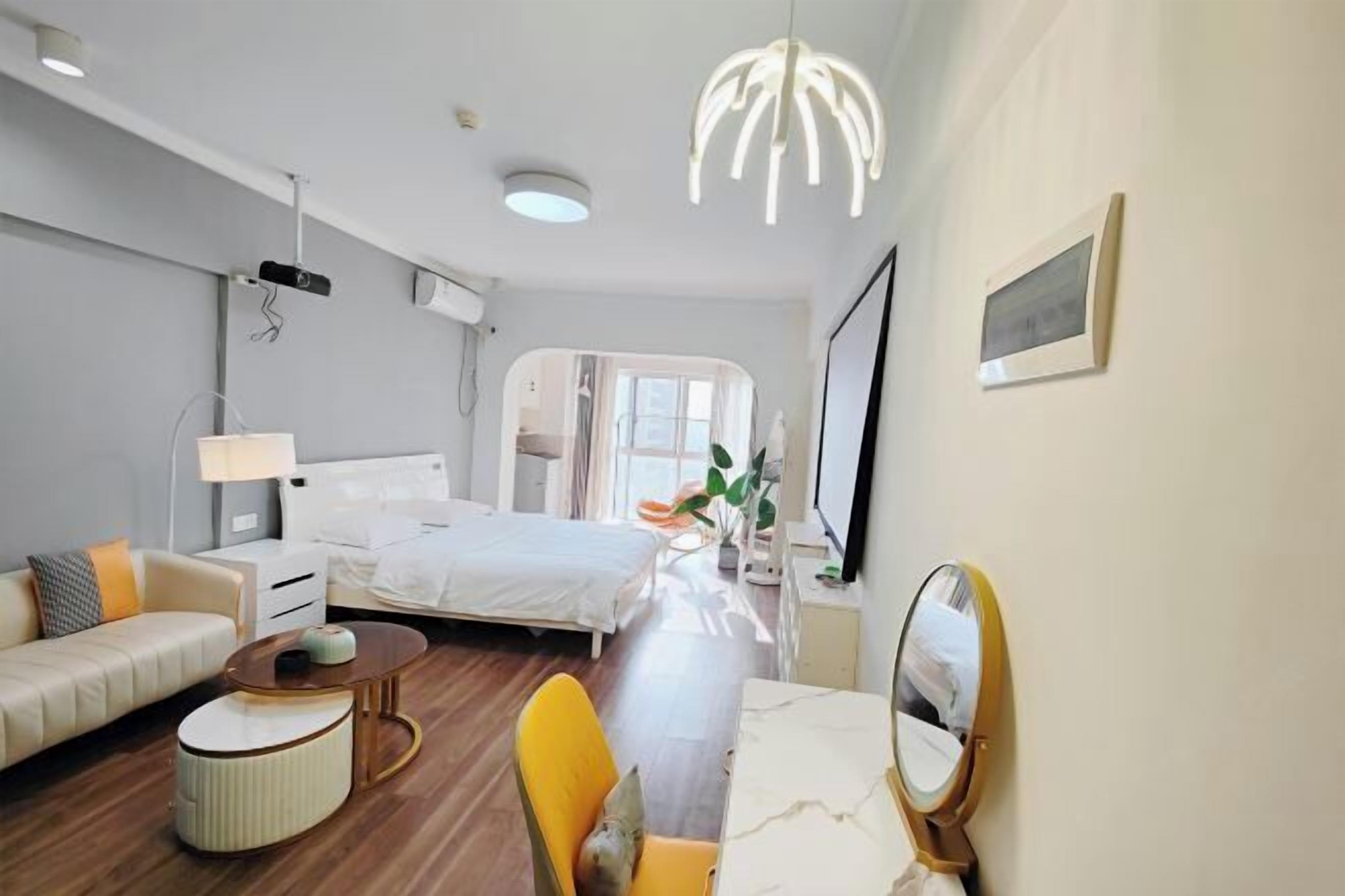 A modern hotel room with a bed, a sofa, a dining table, and a mirror.
