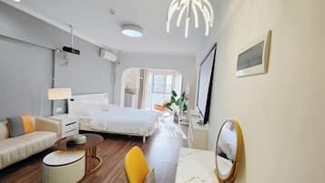 A modern hotel room with a bed, a sofa, a dining table, and a mirror.