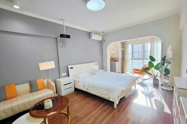 A modern bedroom with a bed, bedside table, lamp, and a sofa.