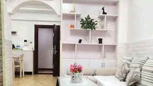 A living room with a white sofa, a coffee table with a vase, and a shelving unit with decorative items. - Shuangshu Apartment Hotel (Changsha Chuangshiji Plaza) (Changsha)