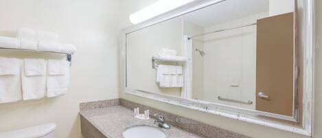 Un baño con un lavabo blanco, un espejo grande y un perchero con toallas dobladas.