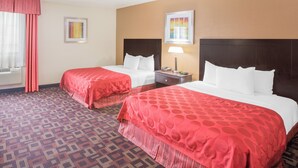 A hotel room with two beds, a nightstand, a lamp, and a window with curtains.