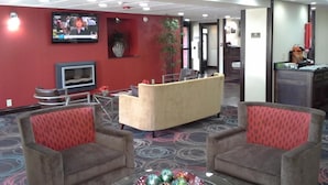 A hotel lobby with a reception desk, two armchairs, a television, and a decorative plant.