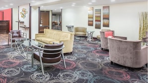 A hotel lobby with a beige sofa, a glass coffee table, and a patterned carpet.