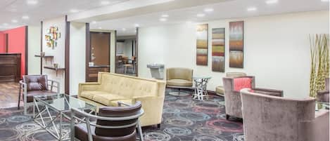 Een hotellobby met een beige bank, een glazen bijzettafeltje en een kamerbreed tapijt met dessin.