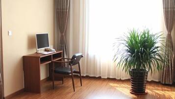 A room with a wooden desk, a chair, a laptop, a potted plant, and a window with curtains.