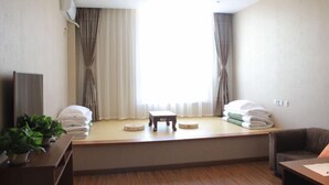 A hotel room with a large window, a small table, a sofa, and a TV on a stand. - Panjin Jingang Business Hotel (Panjin)