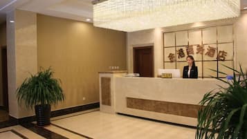 A reception area with a reception desk, a large chandelier, and a potted plant.