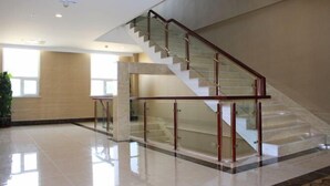 A modern interior with a glass railing staircase, polished floors, and large windows. - Panjin Jingang Business Hotel (Panjin)
