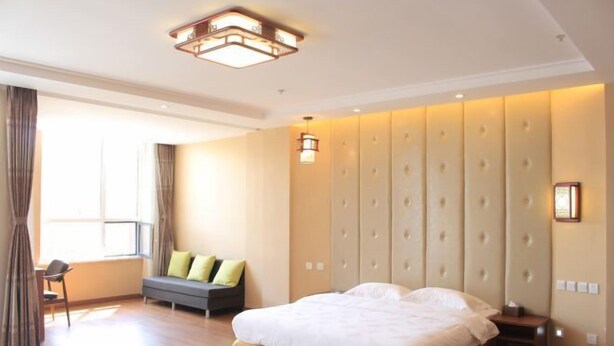A hotel room with a large bed, a sofa, a chair, and a wall with a tufted design. - Panjin Jingang Business Hotel (Panjin)
