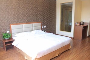 Una cama bien hecha en una habitación de hotel con un cabecero de madera, una mesita de noche con una planta y un ventanal que da a vistas del baño.