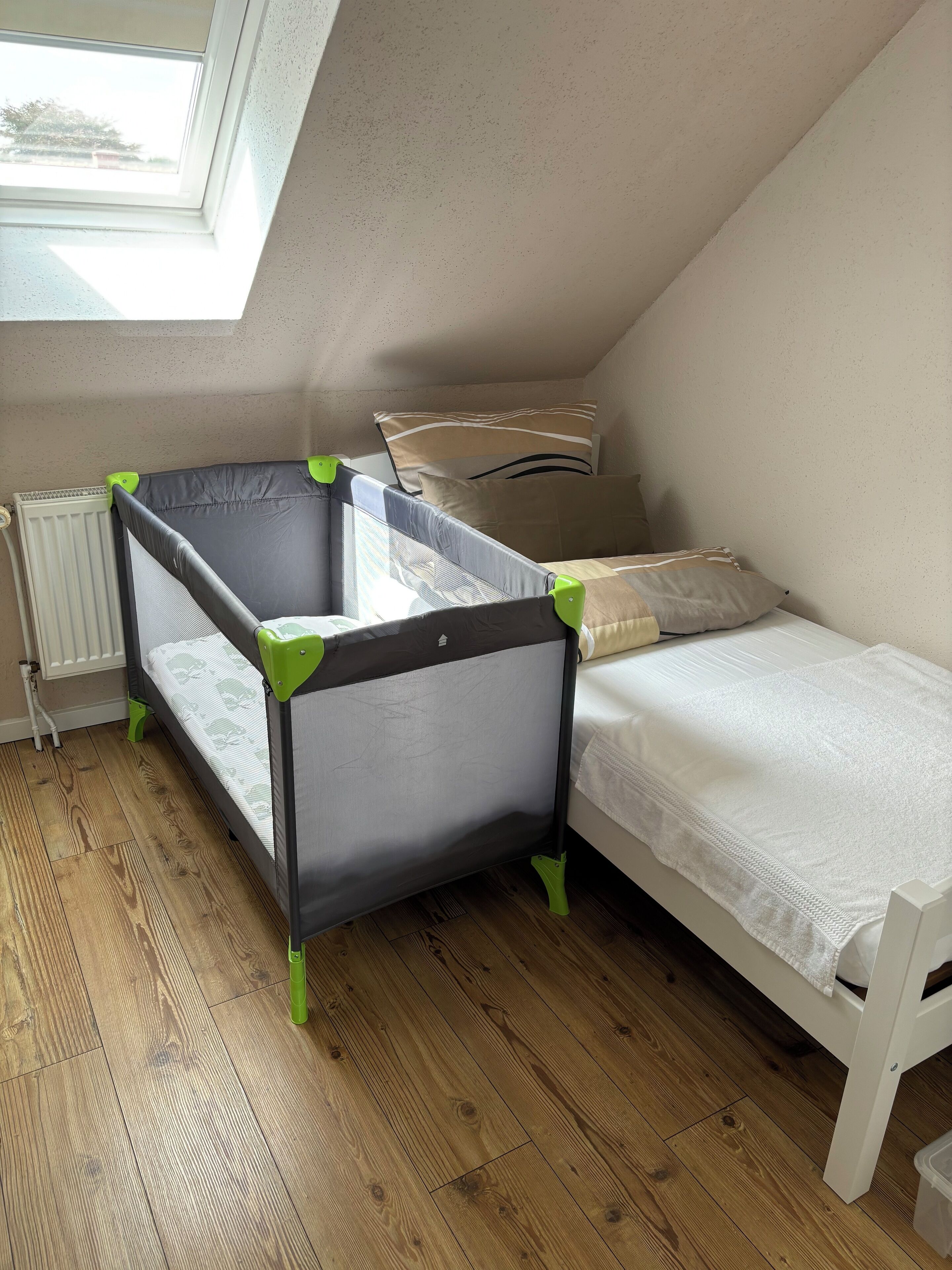 A room with a bunk bed, a single bed, a radiator, and a skylight.