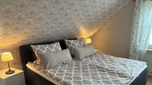 Une chambre à coucher avec un lit, deux lampes de chevet, une table de chevet et une fenêtre avec des rideaux.