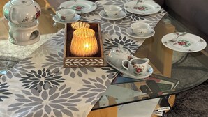 Une table basse avec un plateau en verre, recouverte d’une nappe à motifs floraux, agrémentée d’un service à thé et d’un chandelier allumé.
