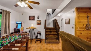 A room with a foosball table, a small bar area, a staircase, and a wooden wall with a guitar.