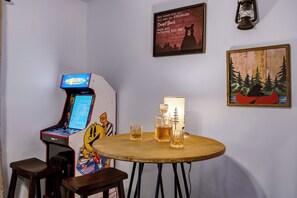 Une pièce avec une table en bois, une affiche sur le thème des ours, une illustration d’ours, une console de jeux vidéo et une bouteille de spiritueux.
