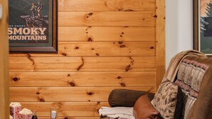A cozy room with wooden walls, a brown leather sofa, a small table with snacks, and a poster of the Smoky Mountains.