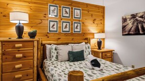 A wooden-paneled room with a bed, two nightstands, a lamp, and framed owl pictures on the wall.