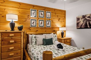 Una habitación con paneles de madera, una cama, dos mesitas de noche, una lámpara y cuadros con lechuzas en la pared.
