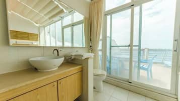 Un baño moderno con un ventanal grande, un tocador de madera, un lavabo blanco y un inodoro.