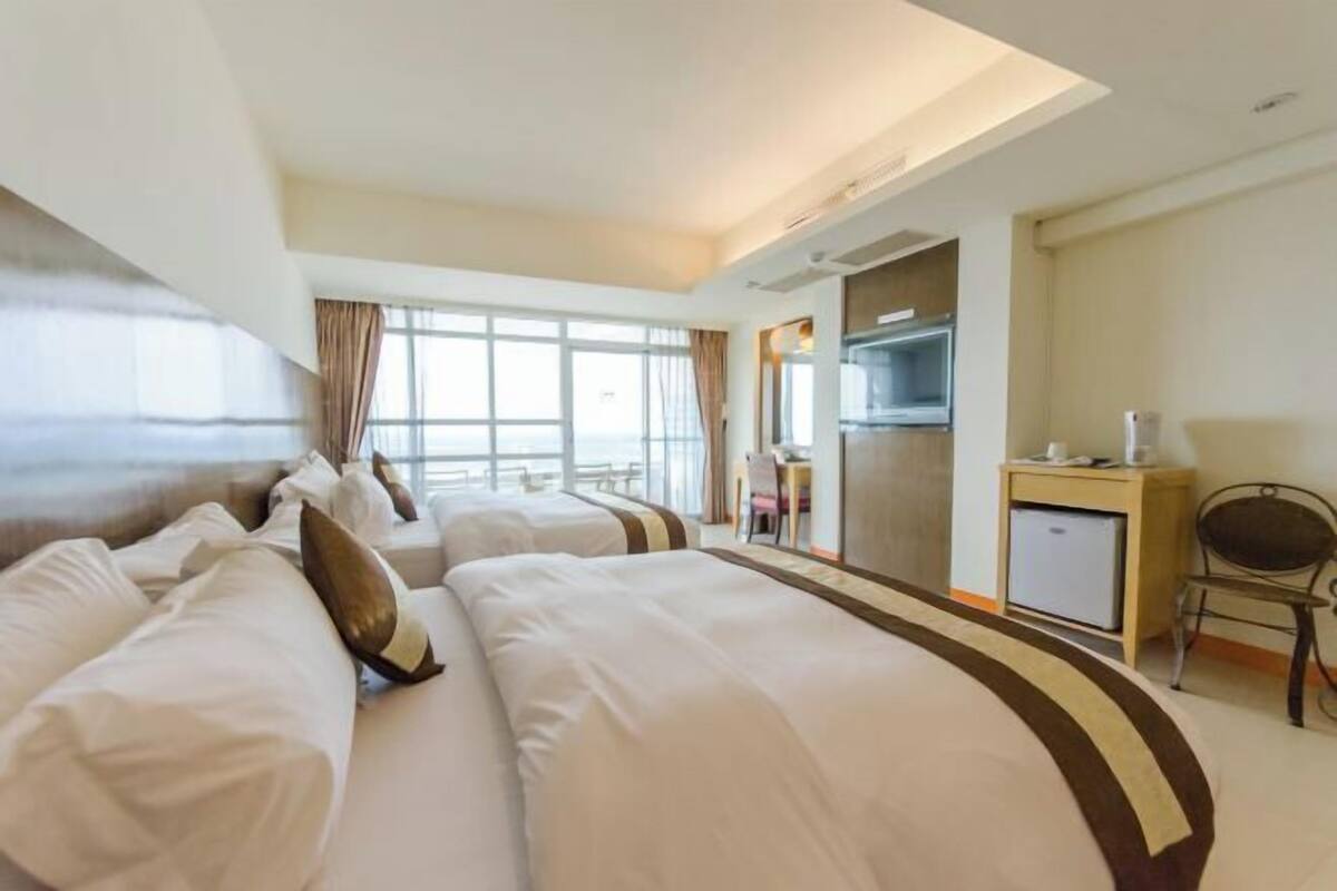 A hotel room with two beds, a desk, a chair, a television, and a small refrigerator.