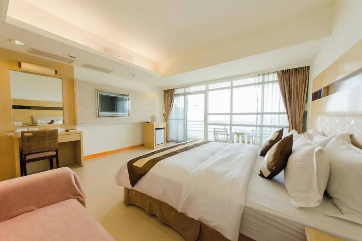 A hotel room with a bed, a desk, a chair, a TV, and a window with curtains.