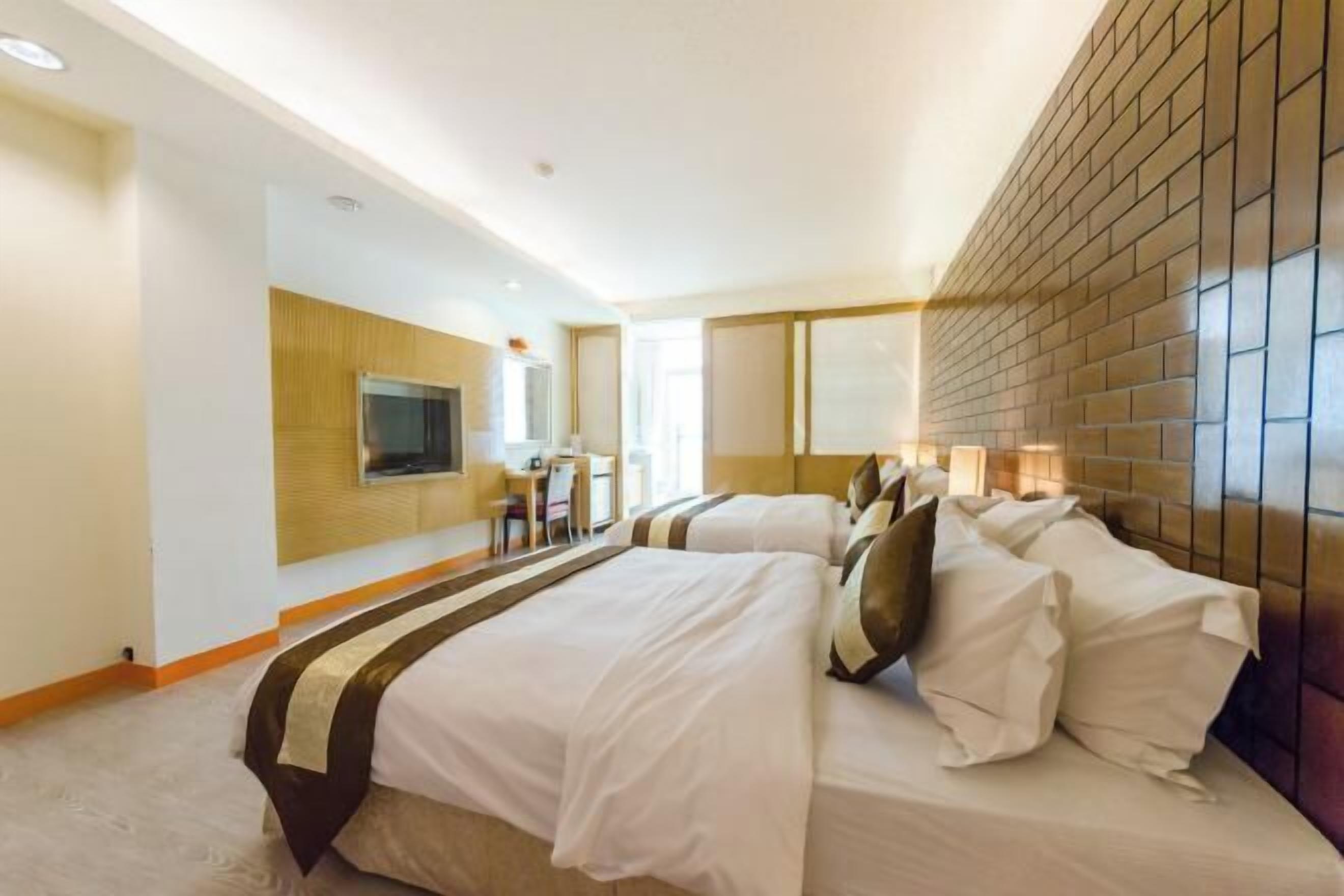 Habitación de hotel con dos camas, televisor, escritorio y pared con diseño de ladrillos.