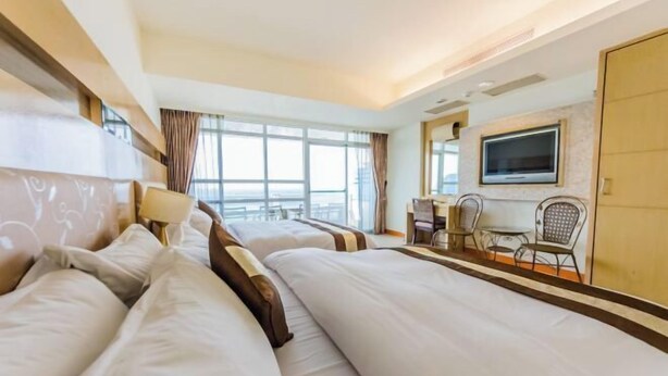 A hotel room with two beds, a desk, a chair, a TV, and large windows. - Yake Hostel (Pingtung)