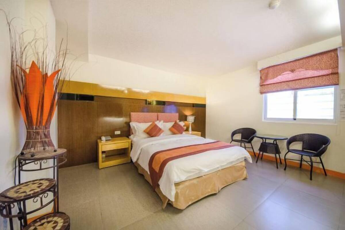A hotel room with a bed, bedside tables, a desk with chairs, and a window with curtains.
