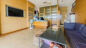 A modern living room with a glass coffee table, a dark sofa, a wooden reception desk, and a TV mounted on the wall. - Yake Hostel (Pingtung)