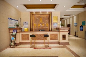 Un mostrador de recepción de hotel con encimera de mármol, dos taburetes de bar y una zona de espera.