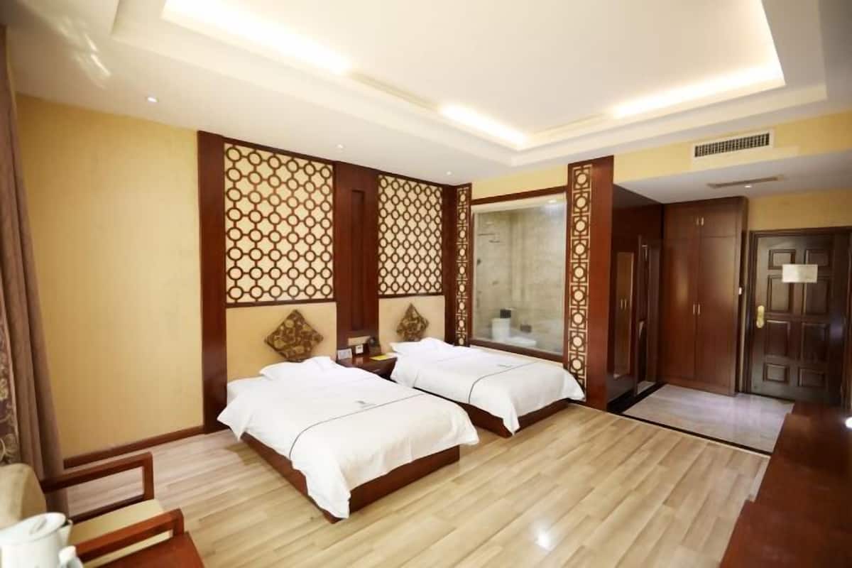 A hotel room with two beds, a wooden floor, a decorative wall panel, a mirror, and a door.