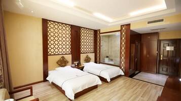 A hotel room with two beds, a wooden floor, a decorative wall panel, a mirror, and a door.