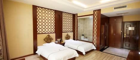 Habitación de hotel con dos camas, piso de madera, un panel decorativo en la pared, un espejo y una puerta.