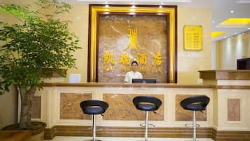 A hotel reception area with a marble counter, a receptionist, and three bar stools.