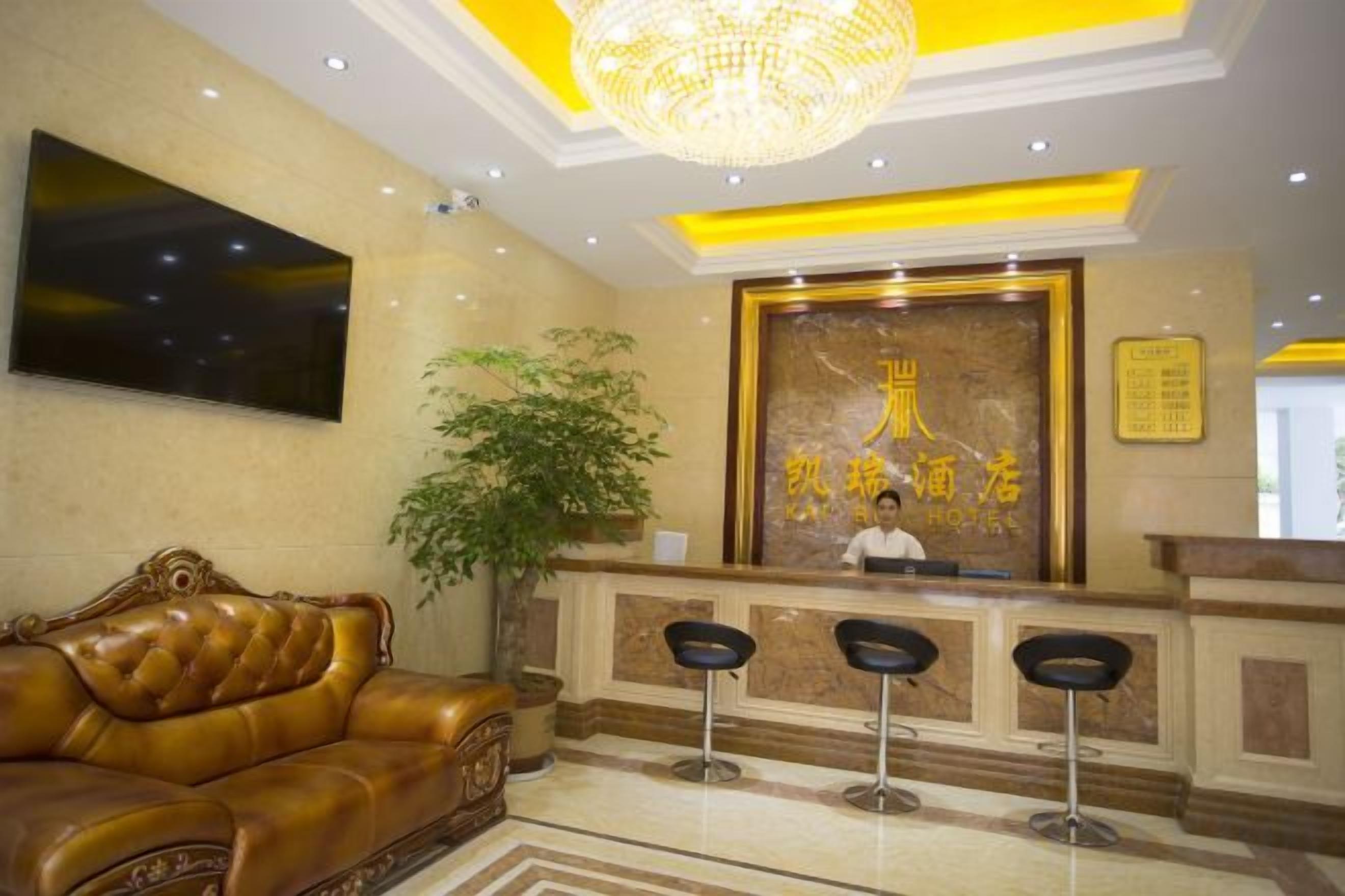 A hotel reception area with a reception desk, a large chandelier, a sofa, and a potted plant.