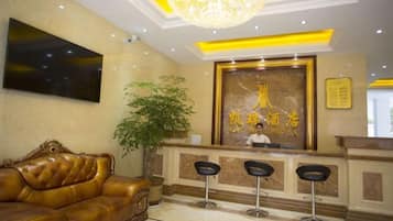 A hotel reception area with a reception desk, a large chandelier, a sofa, and a potted plant.