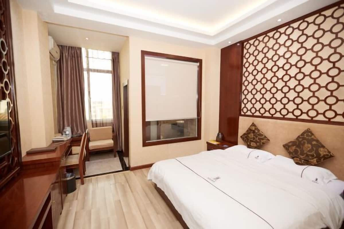 A hotel room with a bed, a desk, a chair, a window with curtains, and a decorative wall panel.