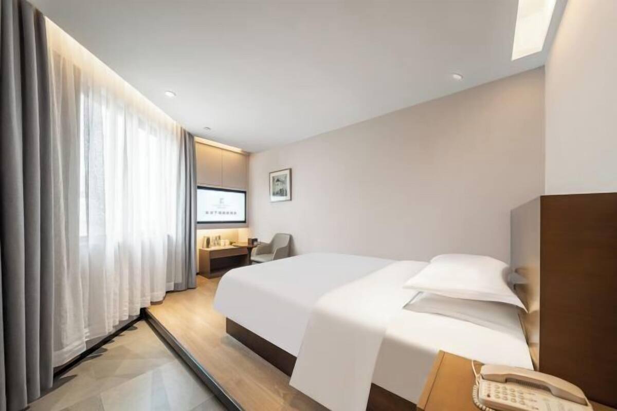 A hotel room with a large bed, a desk with a chair, a telephone, and a television on the wall.
