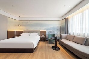 A modern hotel room with a bed, a sofa, a chair, a desk, and a view of mountains through the window. - Ruidu E Hotel (Wenzhou Wuma Street) (Wenzhou)
