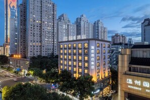 Un hotel de varios pisos con fachada moderna, situado en un entorno urbano con edificios altos al fondo.