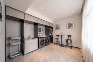 Una cocina compacta con lavadora, un pequeño comedor con taburetes y un estante fijado a la pared.