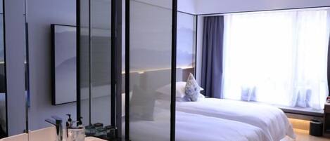 A modern hotel room with a large mirror, a white sink, a bed with white bedding, and a window with curtains.