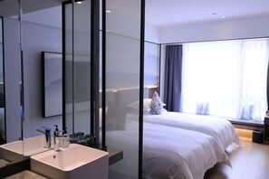 A modern hotel room with a large mirror, a white sink, a bed with white bedding, and a window with curtains.