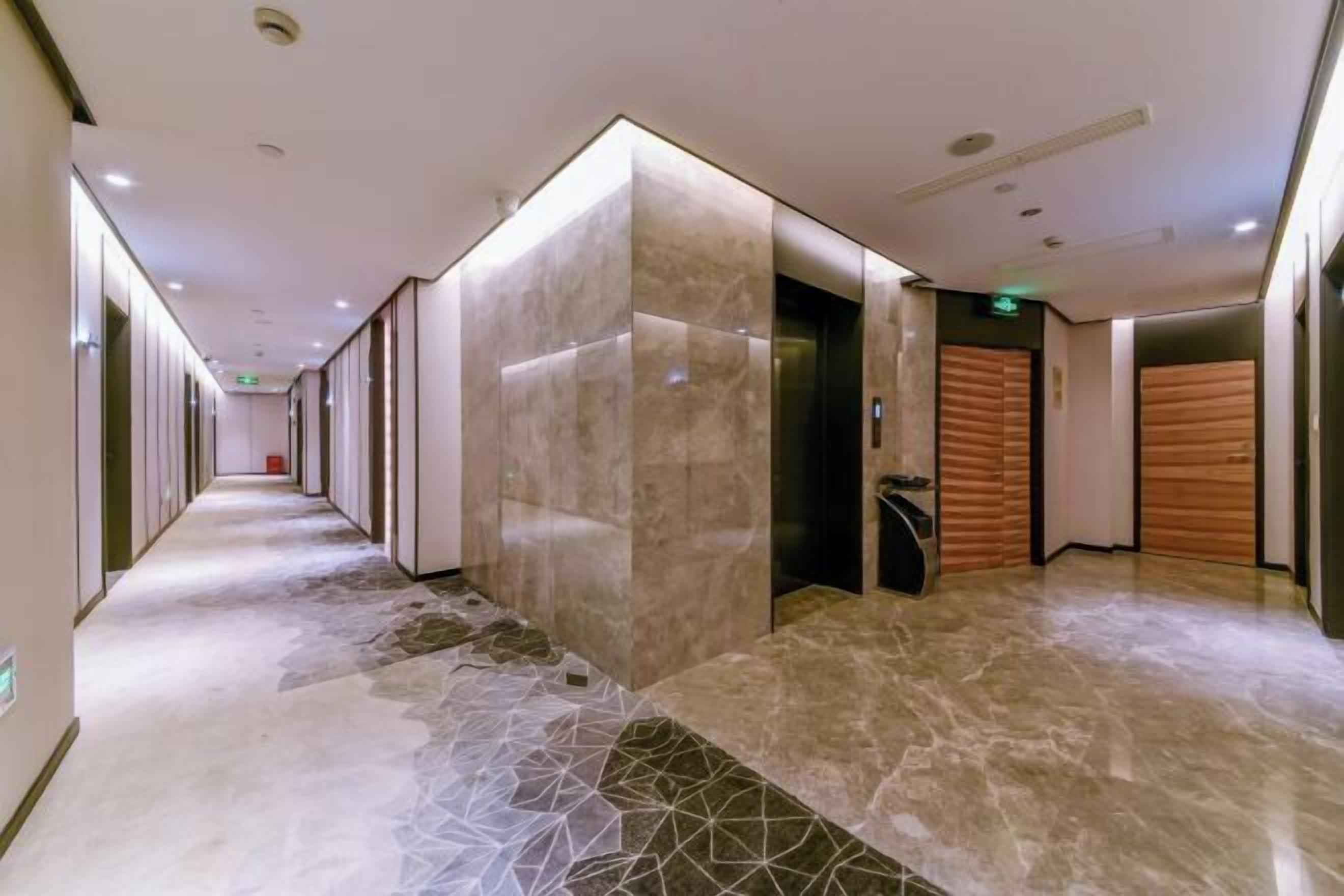 Corredor moderno de hotel com piso de mármore, paredes revestidas de madeira e um elevador.