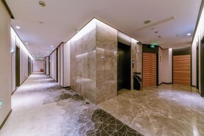 A modern hotel corridor with a marble floor, wooden panel walls, and an elevator.