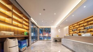 En moderne hotellobby med marmorgulv, reoler med bøger, en reception og en glasdør, der fører udendørs.