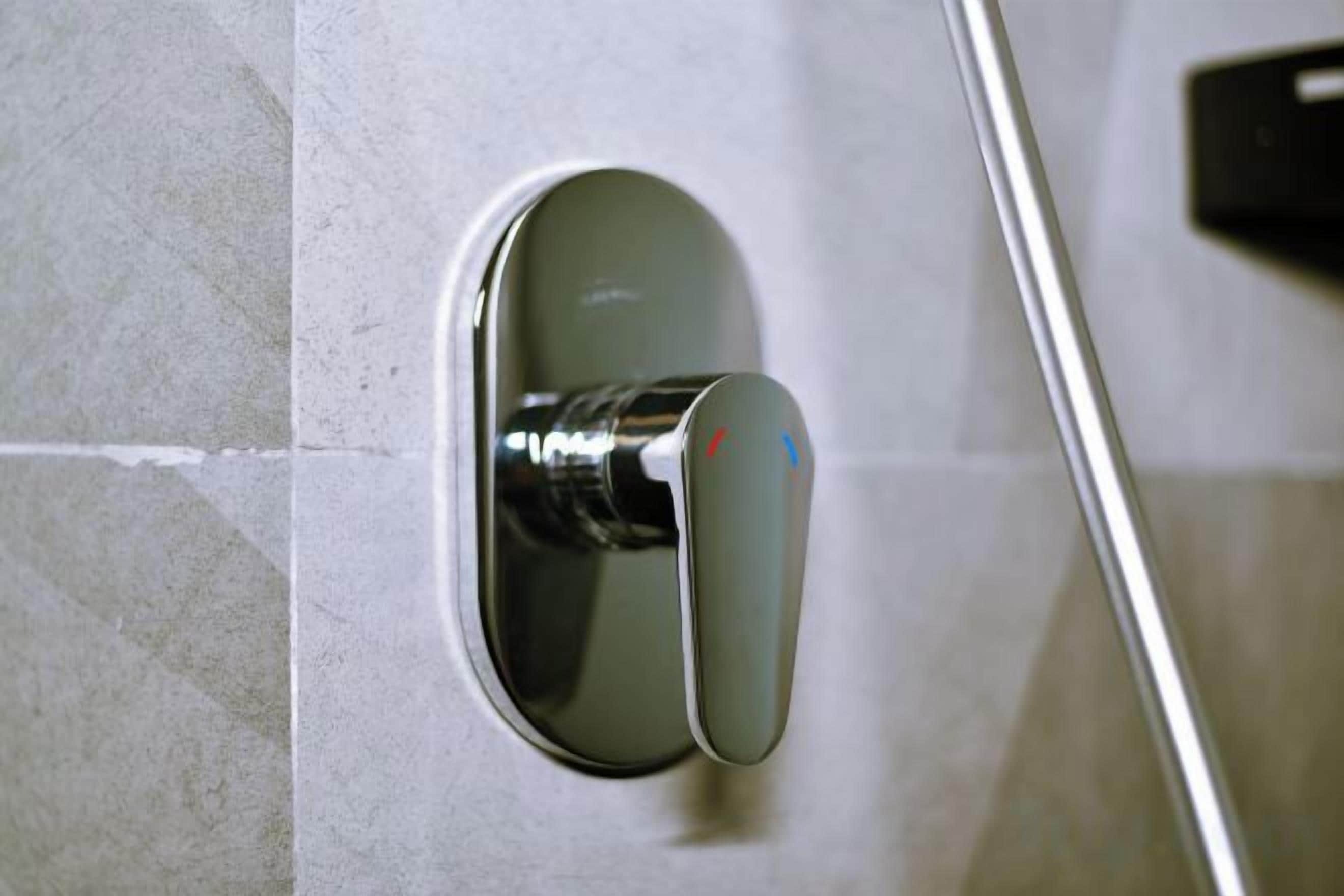 Ein metallener Griff an einer Wand, vermutlich für eine Dusche oder ein Waschbecken.