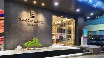 A hotel entrance with a dark facade, a reception desk, and a glass door leading inside.