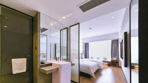Et moderne hotelværelse med en glasbrusekabine, et hvidt håndvask og en stor seng, samt udsigt over byen.